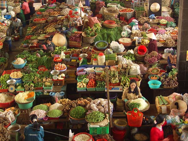 Central Market of Dalat, Vietnam showing brightly colored stalls of fresh fruit and vegetables. Various stall holders are arranging their foodstuffs for sale.