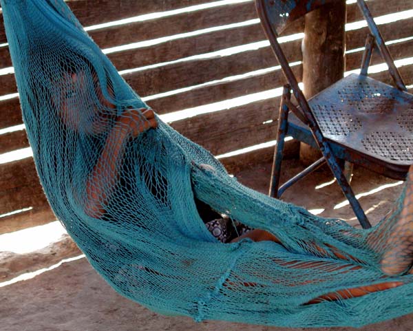 A child of the Amazonas is hiding in a blue string hammock in her house. She is interested in the strangers that have come to visit, but does not want to be noticed herself.